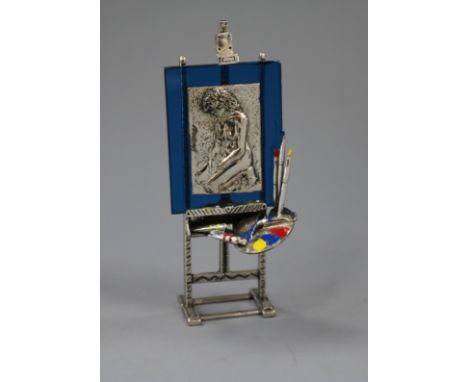 An Italian post 1968 800 white metal, enamel and glass model of an easel, with pallet and portrait, 10.3cm.