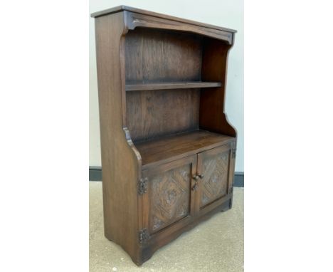 An Old Charm style oak bookcase cupboard, two tiers of open shelving to top, pair of carved cupboard doors to base, enclosing