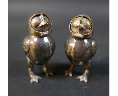 A pair of silver plated pepperettes, early to mid 20th century, in the form of chicks with fold over headscarf covers, 5cm ta