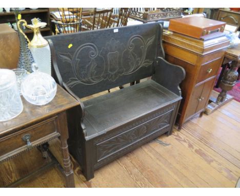 An oak monks bench, the hinged top with lunette carving and cartouche with scrolls to the back over a seat with hinged top an