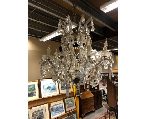 A TWELVE LIGHT CHANDELIER, THE CANDLE LIGHTS ON GLASS CLAD ARMS RISING UP TO FORM THE UPPER TIER, ALL HUNG WITH BEAD SWAGS AN