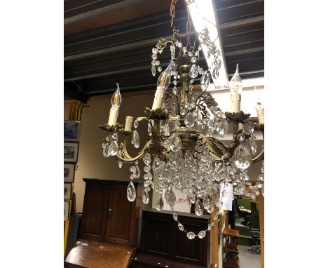 AN EIGHT LIGHT ORMOLU AND GLASS CHANDELIER, THE ARMS BELOW THE UPPER TIER CAST WITH LEAVES, BEARING CANDLE LIGHTS AND HUNG WI