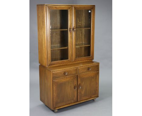 An Ercol elm tall glazed cabinet, the upper part fitted two glass shelves enclosed by a pair of glazed doors, the base fitted