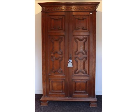 A 17th century-style tall oak wardrobe with a moulded cornice, enclosed by a pair of panel doors with applied geometrical mou