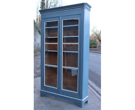 A pale blue &amp; white painted pine tall bookcase with a moulded cornice, having six adjustable shelves enclosed by a pair o