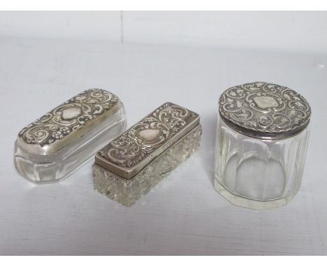 Two Hallmarked Silver Lidded Glass Dressing Table Pots, each detailed in relief with leaf scrolls; together with another trin