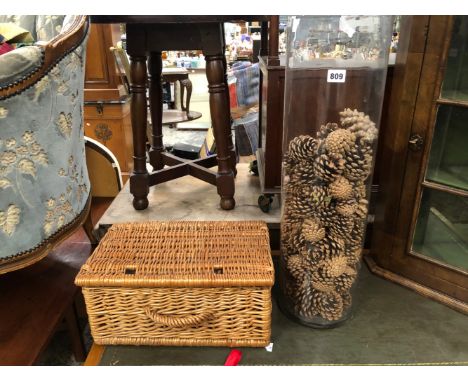 A LARGE GLASS VASE CONTAINING PINE CONES AND A WICKER HAMPER. 