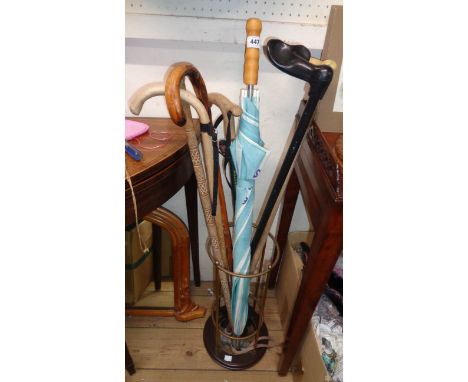 A brassed metal and polished wood stick stand containing a selection of modern sticks and an umbrella