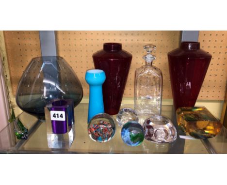 SHELF OF DECORATIVE COLOURED GLASSWARES INCLUDING PAPERWEIGHTS, RUBY VASES AND A RESIN PURPLE CUBE VASE