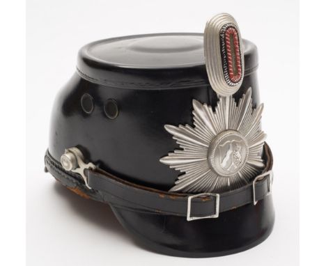 A German Police shako helmet:, black bodied with aluminium star and cockade, side fixings and leather strap, the brown leathe