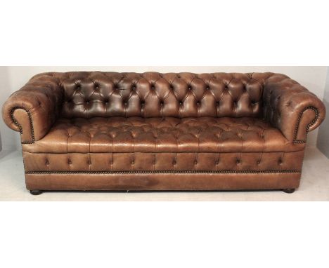 A CHESTERFIELD SOFA, upholstered in brown leather with close-button brass nailing, the deep buttoned back and seat flanked by