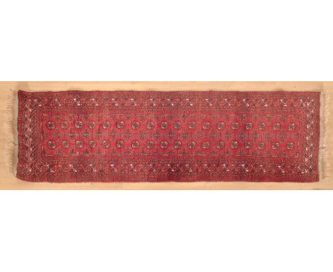 A TEKKE BOKHARA RUNNERthe central panel set with two rows of repeating stylised elephant foot medallions on a red ground with