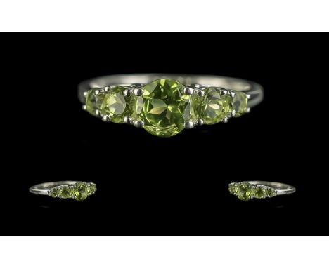 Peridot Five Stone Ring, the peridots graduated from either side of the largest, raised, round cut to the centre; set in rhod