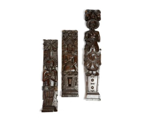 Three carved oak terms, one of an exotic lady playing a mandolin with a fruit surmount, the other two carved with a man and a