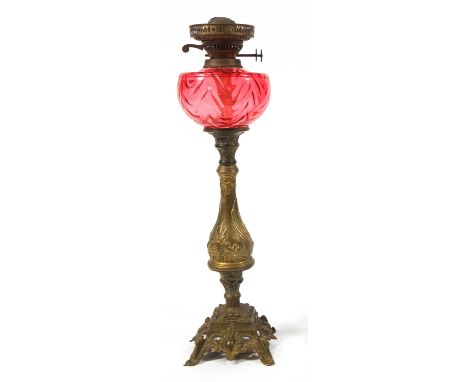 A gilt metal oil lamp with cranberry tinted glass reservoir, 79cm high