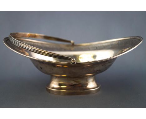 A silver small scale swing handled cake basket, of oval form, with applied reeded edge, highlighted with bright cut scroll de