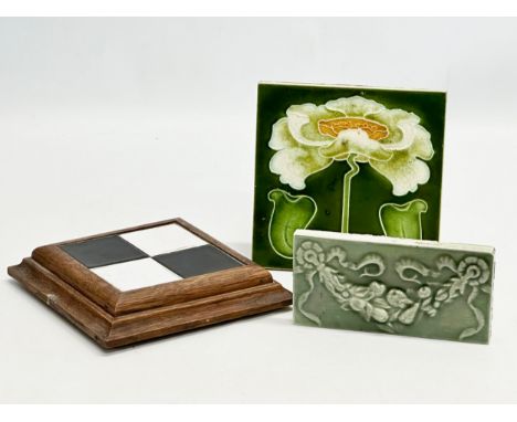 Three Late 19th and Early 20th Century tiles. An Art Nouveau tile 15cm. An oak framed tile top pot stand 17x17x3cm. An Art No