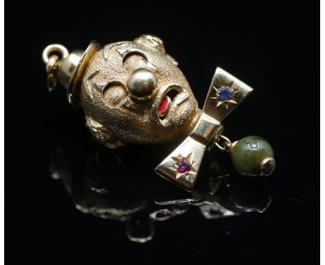 A yellow metal (tested as 9 carat) novelty articulated clown head pendant. The clowns bowtie set with a synthetic ruby and sa