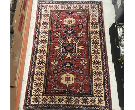 A 20th Century Afghan woollen rug, the central panel set with geometric medallion on a red ground with stylised foliate decor