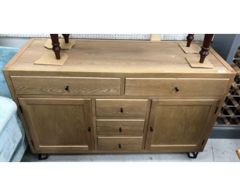 A Cort light oak dwarf sideboard with plain top over two long drawers and three central short drawers, flanked by two cupboar