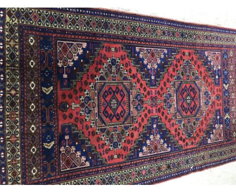 A Persian rug, the central panel set with two repeating medallions, each set with a stylised tarantula motif on a red and blu