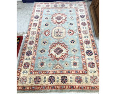 An Afghan Kazak rug, the central panel set with square and lozenge medallions on a pale blue ground, within a stepped red, cr