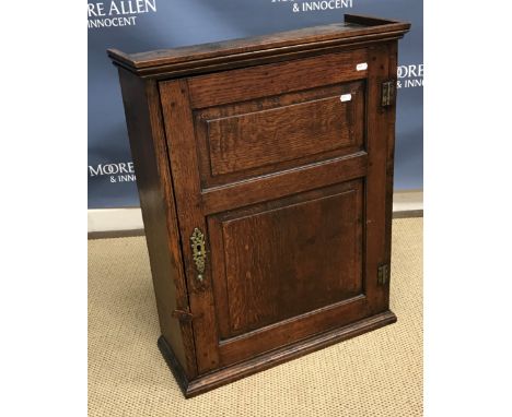 A 19th Century oak wall cupboard, the top with moulded cornice over a twin fielded panel door opening to reveal three shaped 