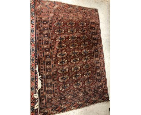 A Tekke Bokhara rug, the central panel set with three rows of elephant foot medallions on a red ground, within a stepped red,