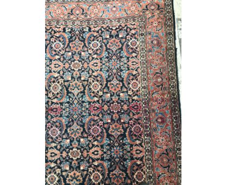 A Persian rug, the central panel set with all-over floral decoration on a dark blue ground, within a stepped orange and faun 
