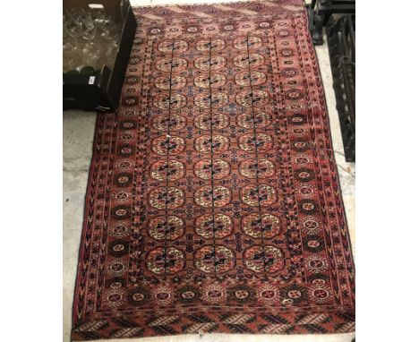 A Tekke Bokhara rug, the central panel with elephant foot medallions on a rust coloured ground, within a stepped stylised tar