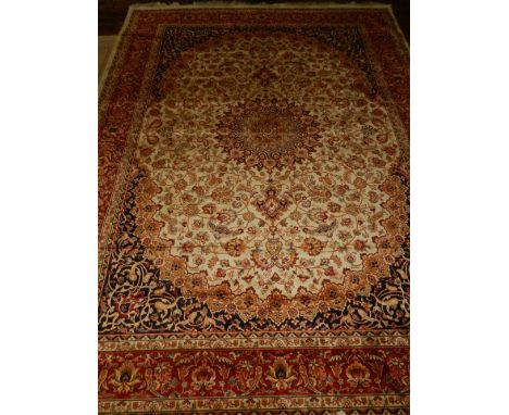 A beige ground Kashan style carpet, having central medallion on a foliate ground, multi-bordered and fringed. L.280cm W.200cm