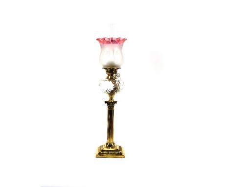 A Duplex brass corinthian column oil lamp, having moulded glass reservoir and ruby tinted shade, 78cm high overall