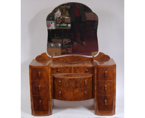 An Art Deco figured walnut dressing table, having a bevelled shaped swing mirror over central hinged drawers, to two further 