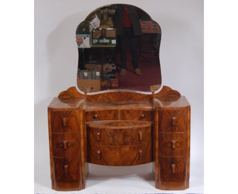 An Art Deco figured walnut dressing table, having a bevelled shaped swing mirror over central hinged drawers, to two further 