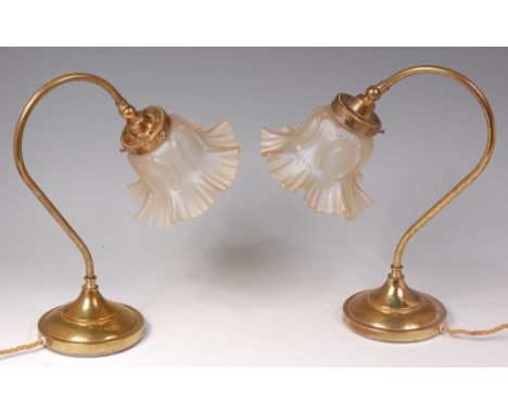 A pair of Art Nouveau brass table lamps, each having shaped floral frosted adjustable shades, raised on curved stems to integ