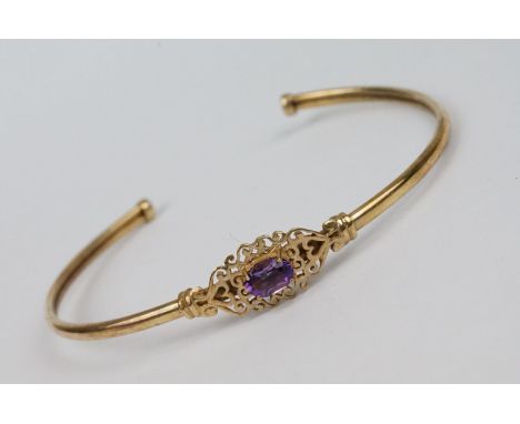 Amethyst 9ct yellow gold bangle, the oval mixed cut amethyst measuring approx 7mm x 5mm, four claw setting with pierced scrol