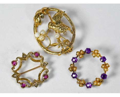 Three open circlet brooches including a 9ct yellow gold oval brooch featuring bird with seed pearl berries, a purple stone an