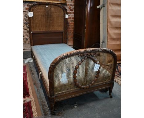 A pair of antique French beech and oak single beds, with arched heads centred by ribbon tie reeded moulding and caned panels,