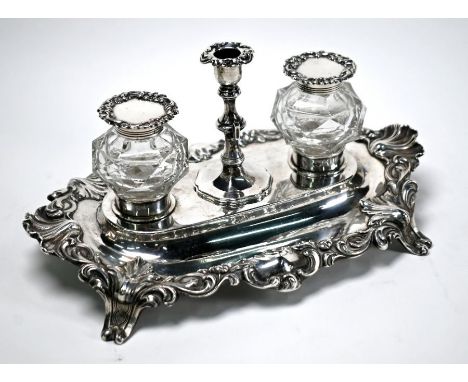 A Victorian Rococo Revival silver inkstand with detachable taperstick enclosing knib-well, flanked by facetted cut glass bott