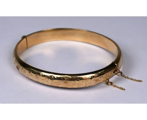 A 9ct yellow gold oval half hinged bangle with chased decoration, concealed clasp and safety chain attached, approx 12g