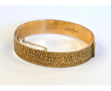 A 9ct yellow gold half hinged bangle with textured bark decoration, concealed clasp with safety chain, approx 24g