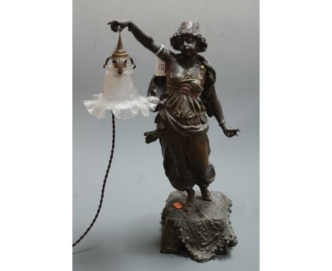 An early 20th century Spelter figural table lamp, in the form of a female carpet seller in standing pose with outstretched ar