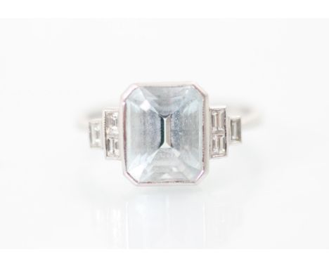 An Art Deco style aquamarine and diamond ring, the central emerald cut aquamarine in rub over white metal setting edge, with 