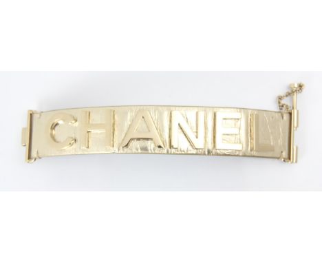 A Chanel leather bracelet, the light gold toned cuff with applied CHANEL lettering, with slide lock clasp, etched Chanel mark