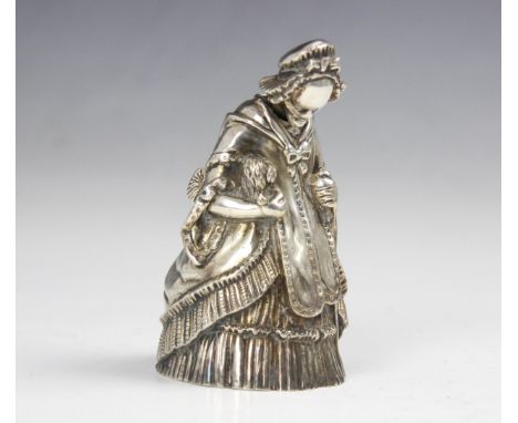 A 20th century white metal novelty table bell, modelled as a well-dressed lady holding a dog and walking stick in other hand,