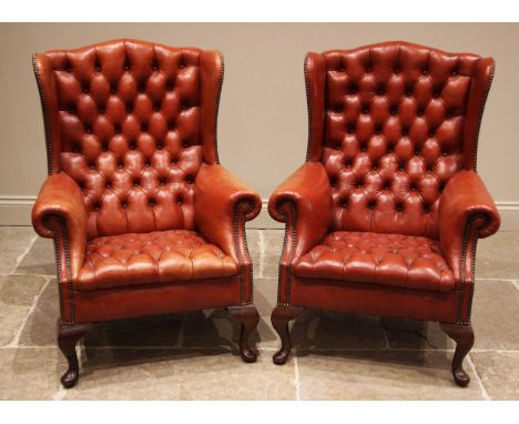 A pair of George III style red leather wingback armchairs, mid 20th century, each with a camel back extending to shaped wing 