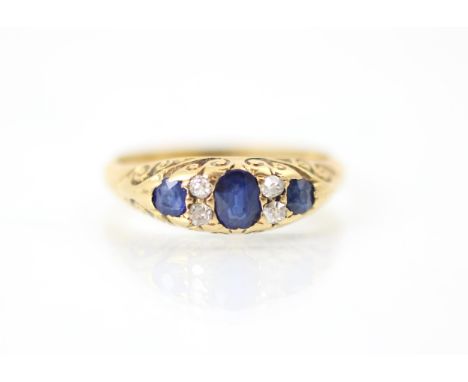 An Edwardian untested sapphire and diamond ring, the central oval cut blue stone with a smaller blue stone to each side, inte