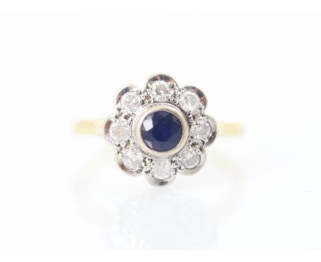 A 20th century style sapphire and diamond cluster ring, the round cut sapphire within white metal rubover mount with a surrou
