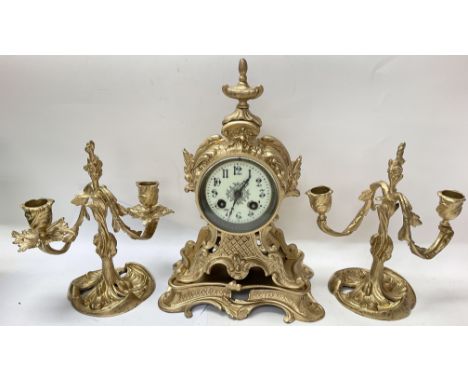 A gilded French mantle clock with a pair of gilded candelabra.