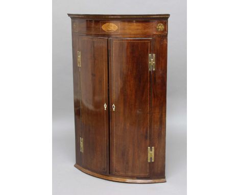 GEORGE III MAHOGANY BOW FRONTED CORNER CUPBOARD, the cornice inlaid with a central oval flanked by roundels above a pair of l